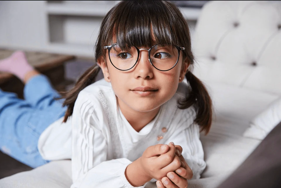 A child wearing round glasses, resting on a cream sofa in the Essilor Stellest campaign